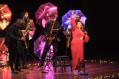 A quarter of saxophonists in black near a singer with one arm in the air. She is in red.