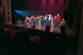 Approximately 15 artists take a bow on stage with audience members seated in the seats in front of them and also on the stage behind them. The photo depicts the final curtain at Perth International Cabaret Festival's closing gala in 2024.