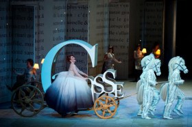 A production on stage with a woman sitting inside a carriage shaped like the letter ‘C’. Opera Australian production.