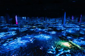 A dark room full of mirrors lit only by the colourful blue and yellow lights scattered in oceanic patterns across the floor.
