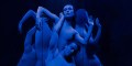 Two contemporary dancers are intertwined in front of a mirror and bathed in blue light.