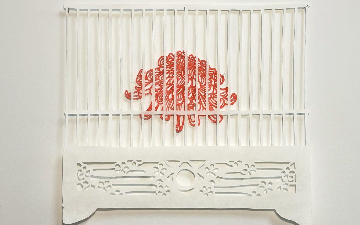 A paper cut artwork of a red chrysanthemum inside a white cage.