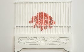 A paper cut artwork of a red chrysanthemum inside a white cage.