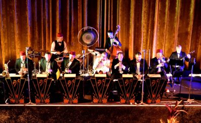 A band scene on stage. Several members are wearing red fez hats.
