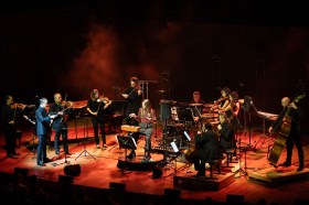 An orchestra on stage with a theremin player seated at their centre.