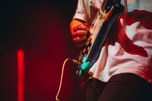 A close-up photo of an electric guitar played by a person wearing a white T-shirt.