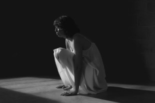 Woman in white dress crouching on floor in shadow, black and white.