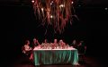 A dinner table set on a small theatre stage with six First Nations women plus one host sitting down and having conversations.