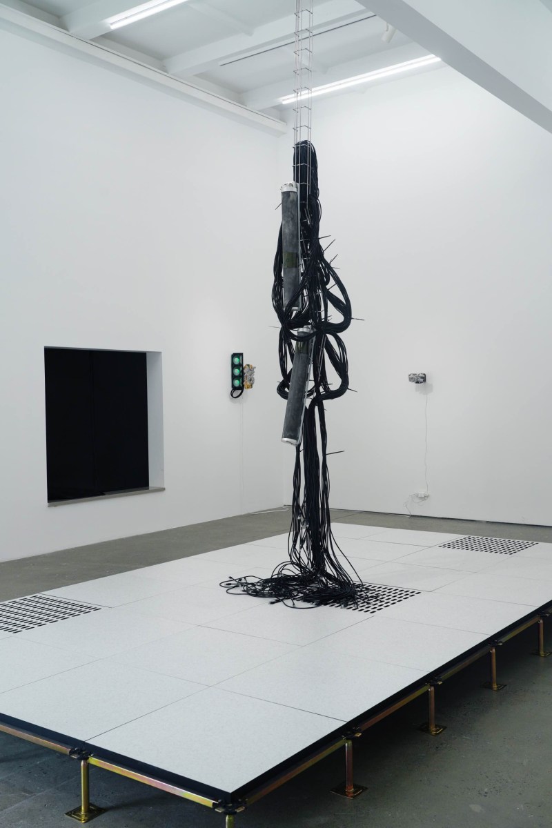 An installation of black tubes hanging from the ceiling in a white gallery space. Art travel.
