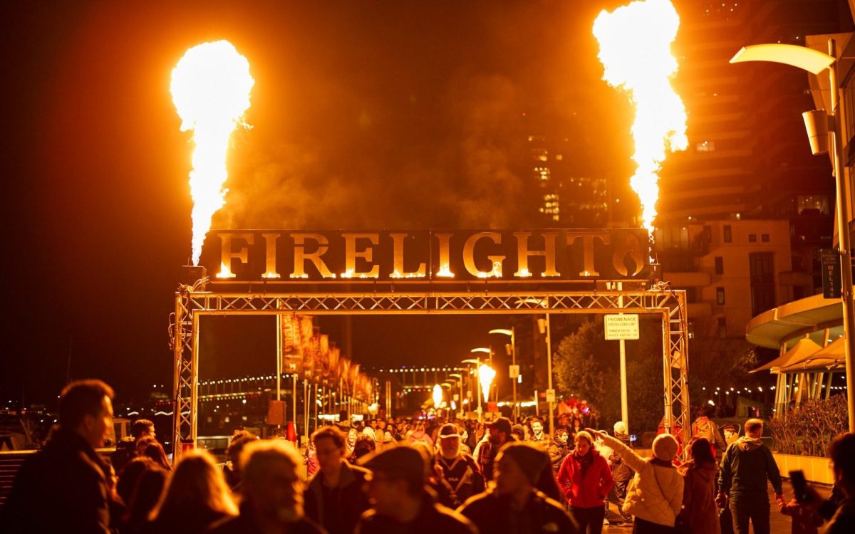 Entrance to an outdoor festival at night with fire on both sides of a large signage with the words ‘FIRELIGHT’.