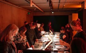 People gathered around a long table looking at material in books and pamphlets in a dark room.