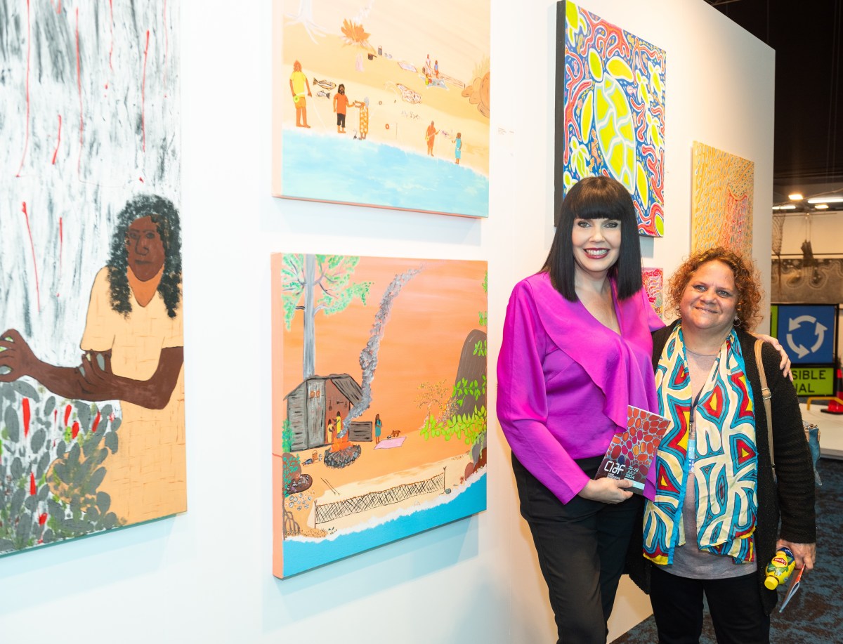 Two people posing for the camera in an embrace, standing in front of paintings. CIAF 2025, ‘Pay Attention!’.