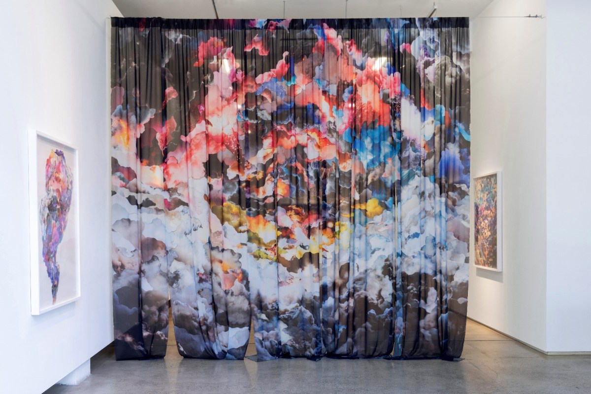 A large hanging curtain printed with coloured collages of protest smoke in an almost swirling pattern, displayed in a white-walled gallery alongside some smaller printed works of the same theme.