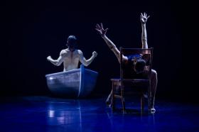 A man is sitting in a boat with his back to us. A woman is sitting on a chair with her face down.