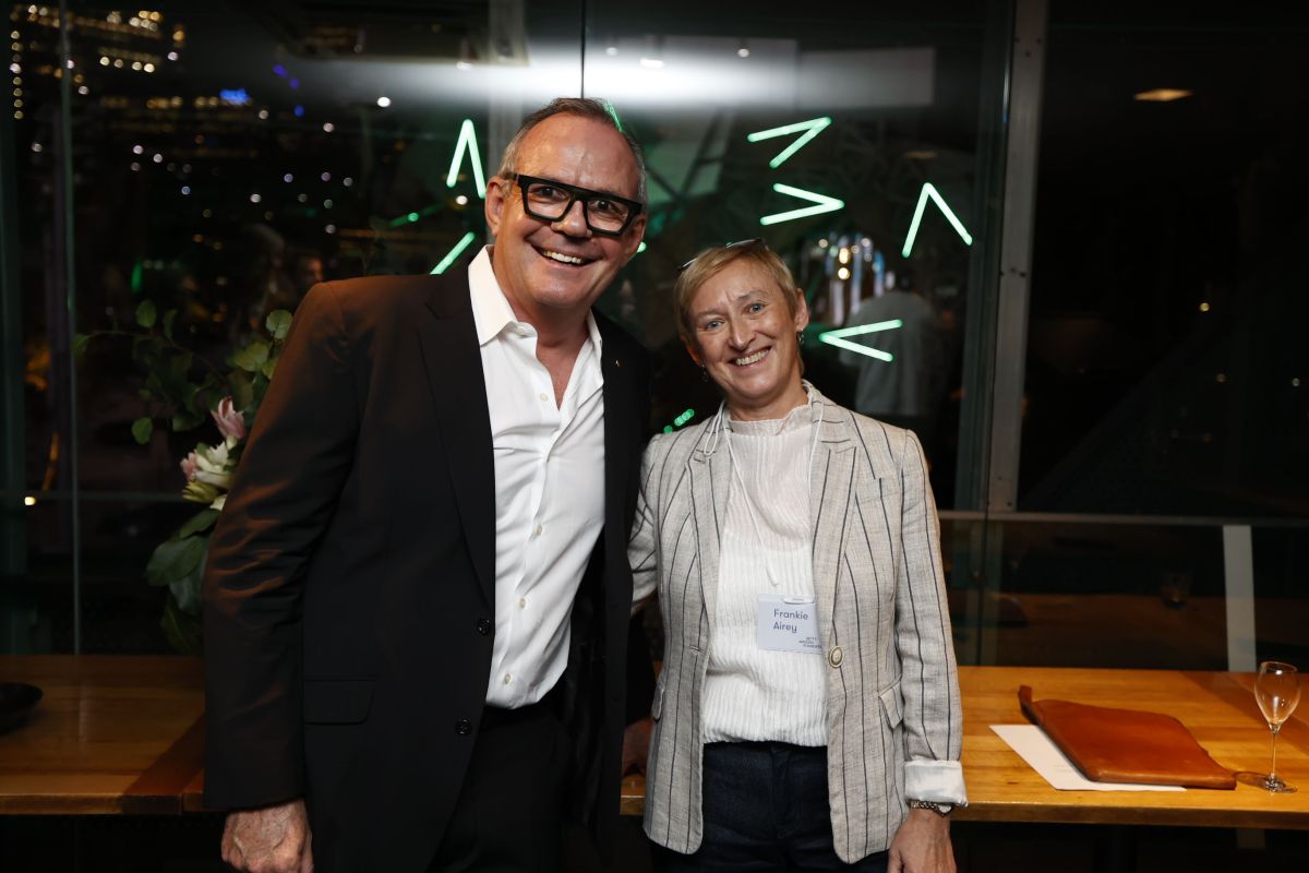 Performing arts legend Richard Evans AM (a middle-aged man wearing bold black glasses and a black suit) with Frankie Airey (a middle-aged woman wearing a stripe linen jacket) posing together and smiling at the camera.