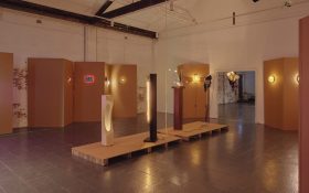An installation of different free standing lights and a few on tan-coloured panels inside a space with high ceiling.