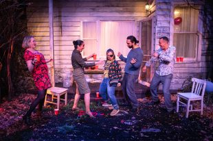 Two young women and three young men are dancing outside a house.
