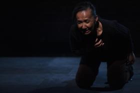 A dark-skinned woman on all fours, grimacing in the dark.
