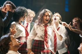 A group of young adults dressed in school uniform of white, red and black. They seem to be taunting a girl in the centre.