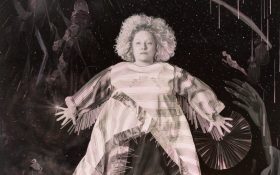 A detailed crop from a painting depicting a woman floating in a dark space with her arms outstretched and objects surrounding her.