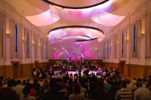 An ANAM performance in a large room. The audience sit facing a pianist and violinists.