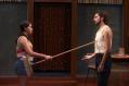 A young woman is poking the handle of a broom at a young man.