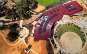 An aerial view of a red, dark red building surrounded by native trees, grasslands and an amphitheatre.