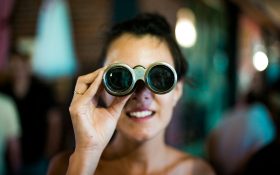 A woman looking through a pair of opera glasses, illustrating our weekly Arts News Watch column.