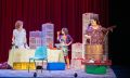 Three women wearing aprons stand in the middle of a kitchen making passata. There are boxes and trays of tomatoes around. A scene from Brink Productions/STCSA's 'Looking for Alibrandi'.