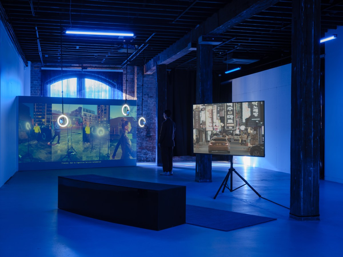 A gallery space with two video screens showing street scenes.