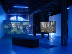 A gallery space with two video screens showing street scenes.