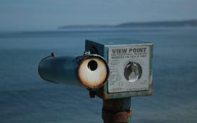 A metal object that looks like a view finder positioned by the water.