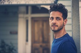 A photo of Lior, who will be at the Adelaide Guitar Festival. He is a young man with olive skin and dark, curly hair. He wears a blue t-shirt.