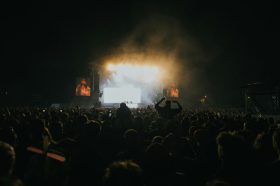 Crowd of music goers in front of a stage in a dark venue.
