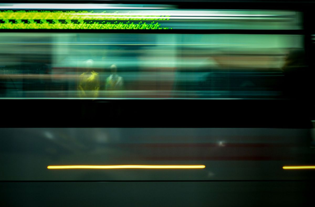 On the move is ArtsHub's weekly round-up of comings and goings in the Australian arts sector. The photograph is a blurred image of a train passing through a station at high speed. The indistinct shapes of two people waiting on the opposite platform are visible through the train's windows.