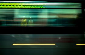 On the move is ArtsHub's weekly round-up of comings and goings in the Australian arts sector. The photograph is a blurred image of a train passing through a station at high speed. The indistinct shapes of two people waiting on the opposite platform are visible through the train's windows.