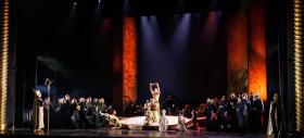 Large stage scene of 'Samson & Delilah'. In the centre are figures wearing gold costumes. They are surrounded by cast in black.