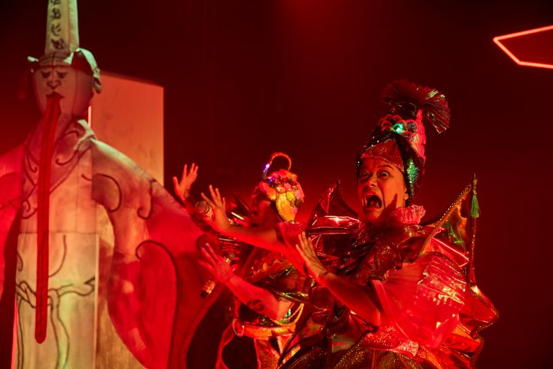 Two actors Asian-Australian actors in elaborate and colourful costumes react in mock-terror at finding themselves in Diyu, the Chinese Hell. An inflatable figure representing one of the guards of Hell is also pictured. A scene from the MTC/RISING production 'Legends (of the Golden Arches)'.