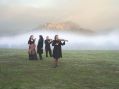 Chamber music ensemble Accademia Arcadia stand in a foggy paddock playing their instruments. The mysterious heights of Hanging Rock rise from the mist and trees behind them. A promotional image for Woodend Winter Arts Festival.