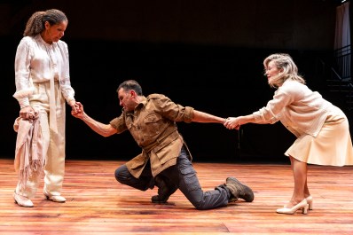 A man in brown is kneeling between two women in white.