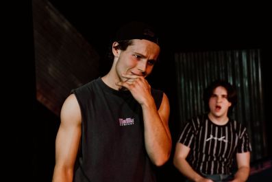 A young man looks shocked while another youth shouts at him in the background. A scene from Lunatix Theatre's 2025 production of 'Blackrock' at The MC Showroom.
