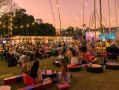 An atmopheric photo of Darwin Festival's Festival Park at dusk, showing festivalgoers dining al fresco under fairy lights and the sunset-streaked sky.