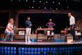 Two men and two women stand beside small work tables.