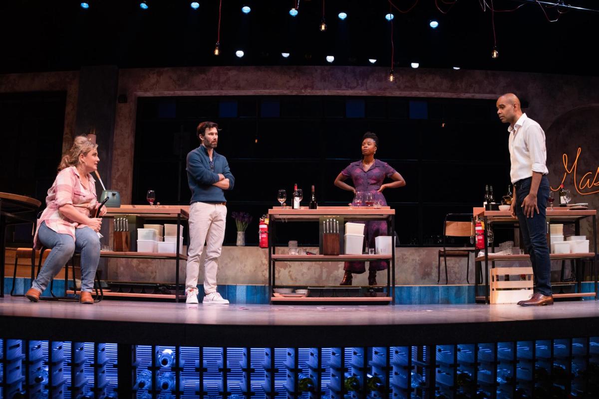 Two men and two women stand beside small work tables.