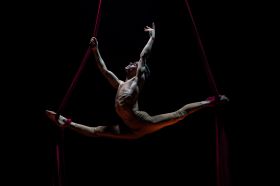 A male acrobat performs the splits, his body held aloft by aerial straps, in a scene from 'La Clique' at Adelaide Cabaret Festival.