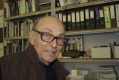 An older balding man with glasses and a brown jacket stands in front of shelves of files. Leo Christie