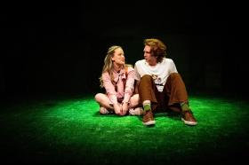 A young woman and man are sitting on a patch of fake grass. Love and Information.