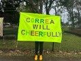Person with yellow sandshoes holding up a banner with text on it about plants. OpenField