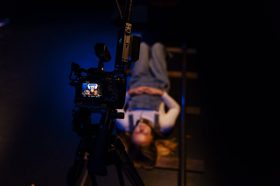 A young girl likes on her back on the floor with a movie camera above her. POV