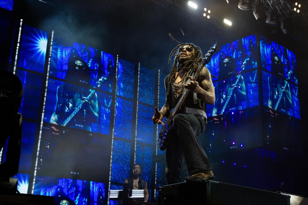 A male guitarist on stage under blue lighting.